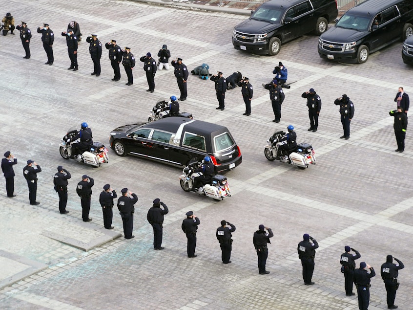 caption: The hearse carrying the remains of Capitol Police officer Brian Sicknick drives past police officers saluting after a funeral ceremony at the US Capitol February 3, 2021 in Washington, DC.
