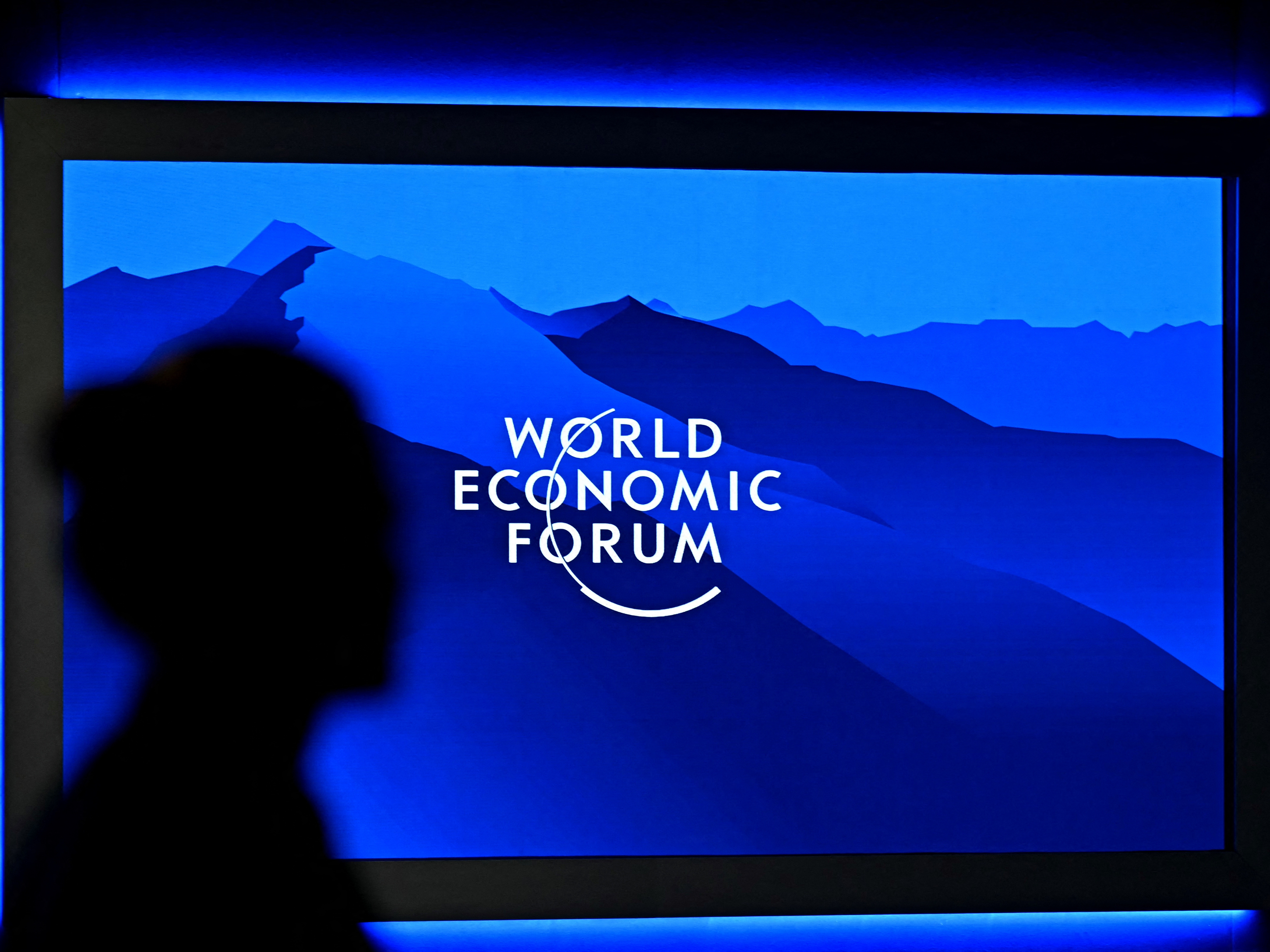 caption: The logo of the World Economic Forum is displayed on a big screen as a visitor is silhouetted during the World Economic Forum (WEF) annual meeting in Davos on Jan. 20.