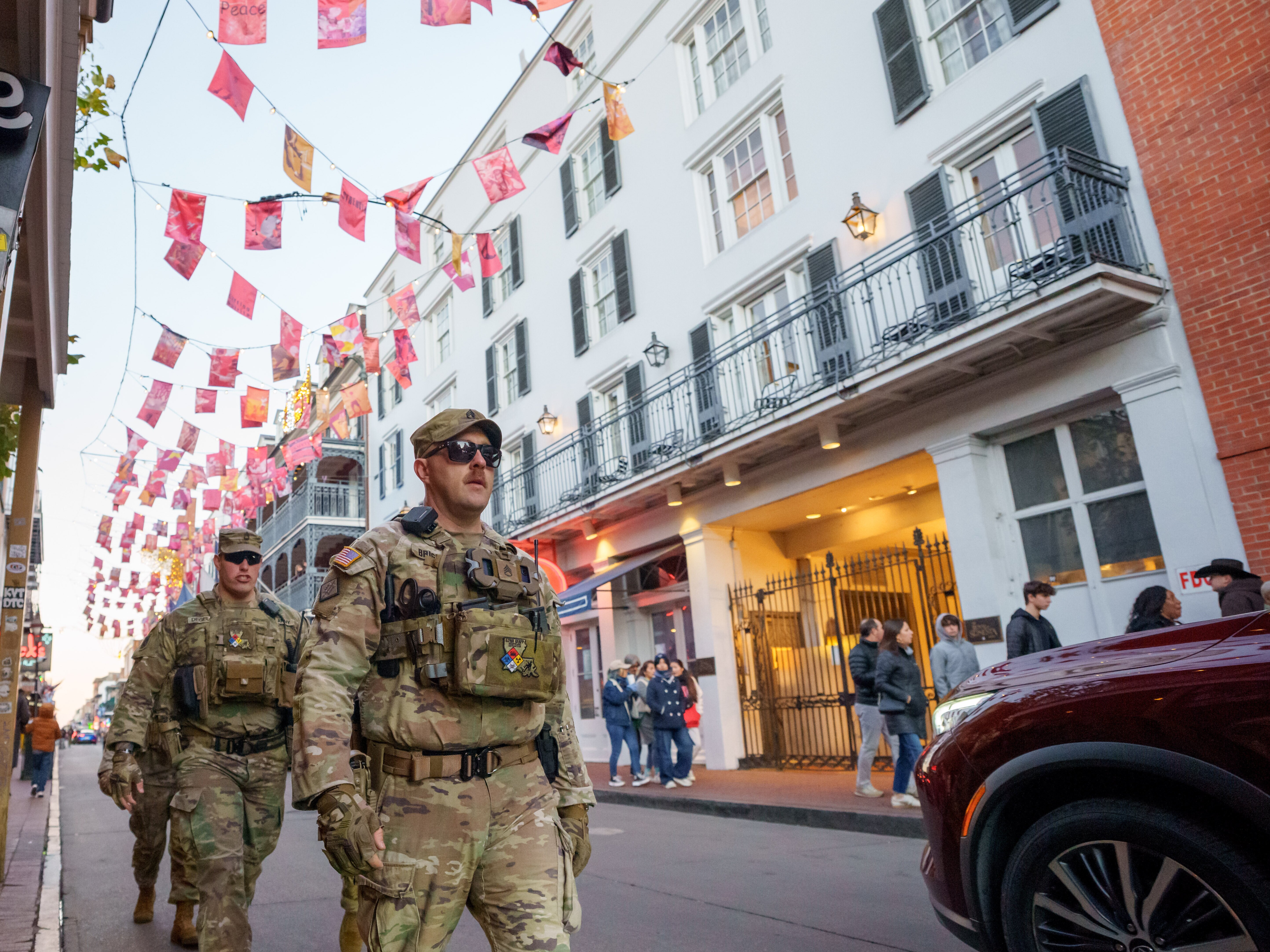 caption: Walking under flags that memorialize victims of Jan. 1, 2025 attack, members of the Louisiana National Guard, military police, and Louisiana law enforcement agencies patrol the French Quarter along Bourbon Street and intersecting streets as part of a National Guard deployment for New Year's celebrations in New Orleans, Tuesday, Dec. 30, 2025. (AP Photo/Matthew Hinton)