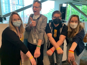 caption: Group photo of four KUOW staff (Bill, Katie, Libby, Dyer) displaying their wristbands.