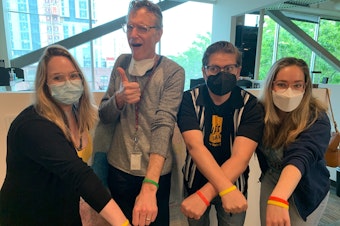 caption: Group photo of four KUOW staff (Bill, Katie, Libby, Dyer) displaying their wristbands.