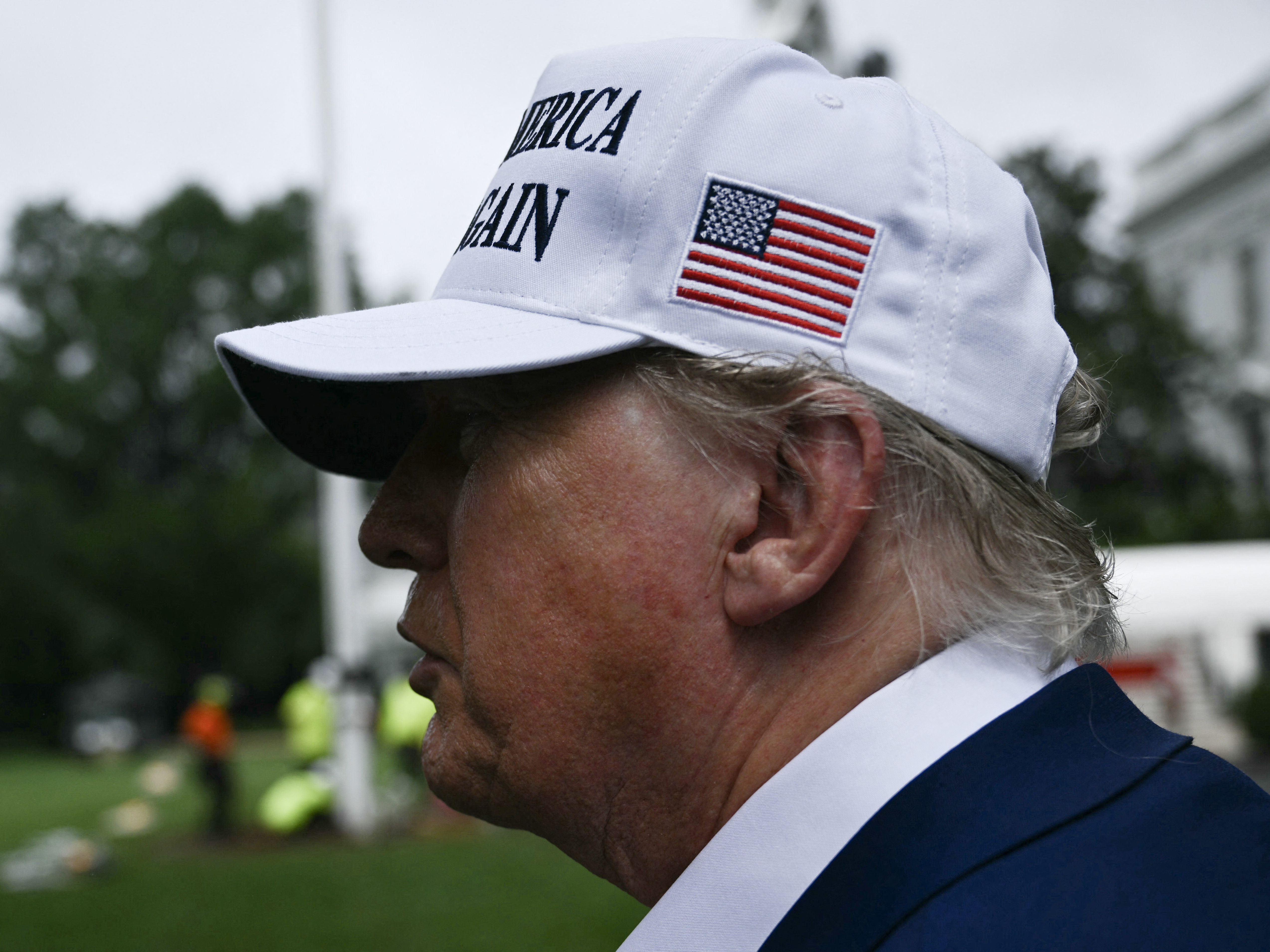 caption: President Trump speaks to the press as workers install a large flag pole on the South Lawn of the White House in Washington, DC on June 18, 2025.