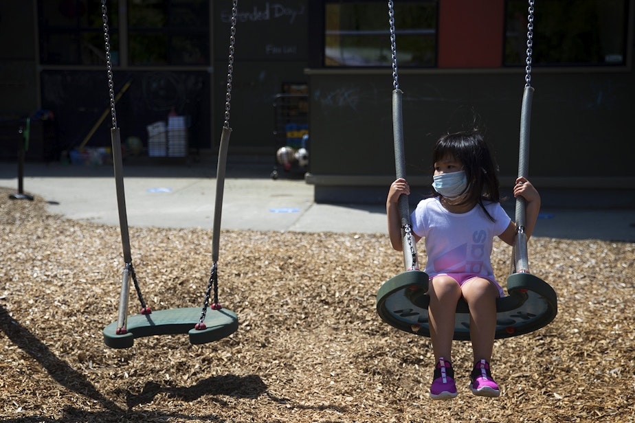 caption: A student at the Denise Louie Education Center swings on a swing set after collecting flowers on a walk with teacher Margarita Arias on Thursday, July 16, 2020, on the playground along Beacon Avenue South in Seattle.