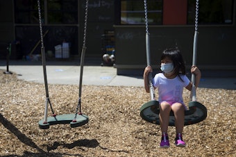 caption: A student at the Denise Louie Education Center swings on a swing set after collecting flowers on a walk with teacher Margarita Arias on Thursday, July 16, 2020, on the playground along Beacon Avenue South in Seattle.