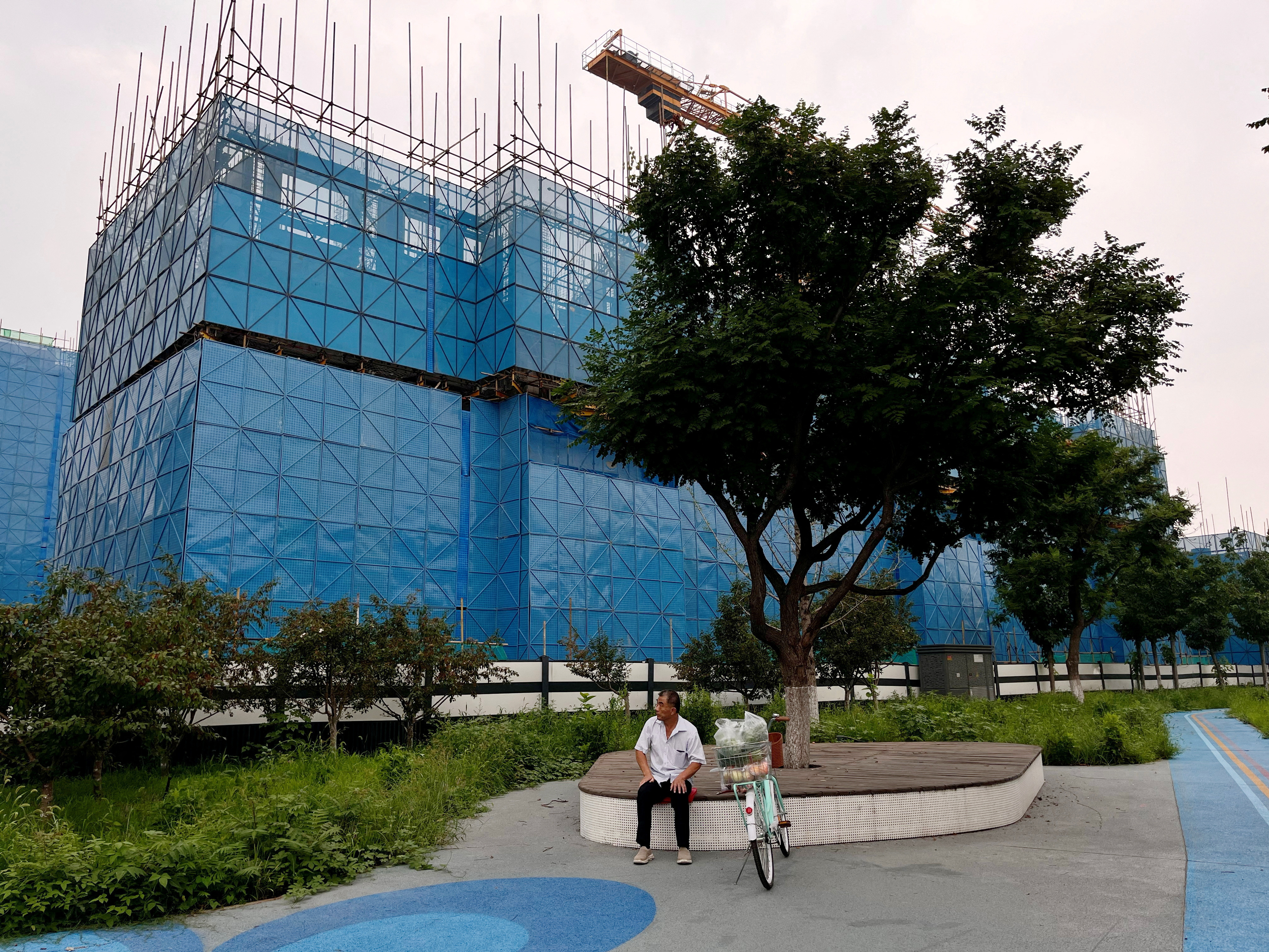 caption: A person sits near a construction site of residential buildings by Chinese developer Country Garden, in Beijing, Aug. 11. Country Garden is facing major financial challenges.