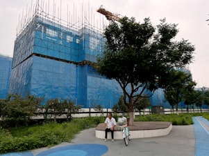 caption: A person sits near a construction site of residential buildings by Chinese developer Country Garden, in Beijing, Aug. 11. Country Garden is facing major financial challenges.