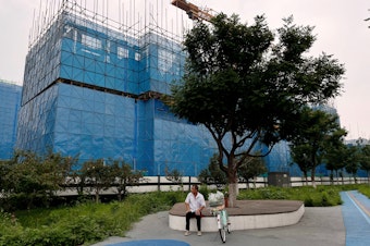 caption: A person sits near a construction site of residential buildings by Chinese developer Country Garden, in Beijing, Aug. 11. Country Garden is facing major financial challenges.