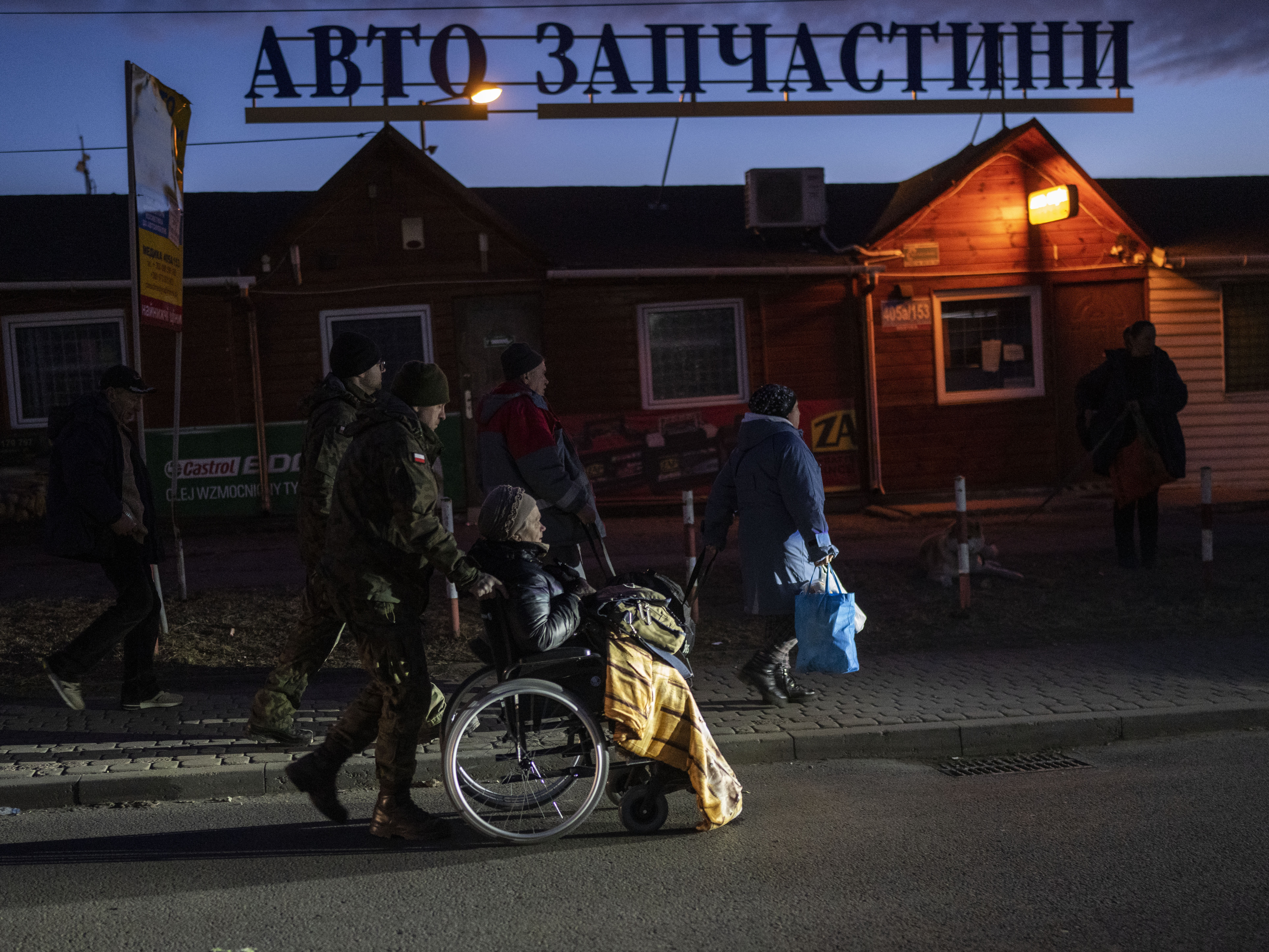 caption: A Polish soldier helps a refugee who fled the war from Ukraine at the Medyka border crossing in Poland, on Saturday, March 12, 2022. Russian troops are pressing their offensive across Ukraine, pounding populated areas with artillery and airstrikes and deploying siege tactics honed in Syria and Chechnya — where opposing cities were reduced to rubble.