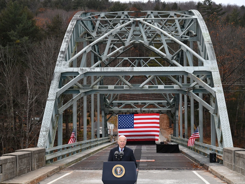 caption: President Biden speaks about his infrastructure bill at a bridge across the Pemigewasset River in Woodstock, N.H., which has been declared structurally unsafe.
