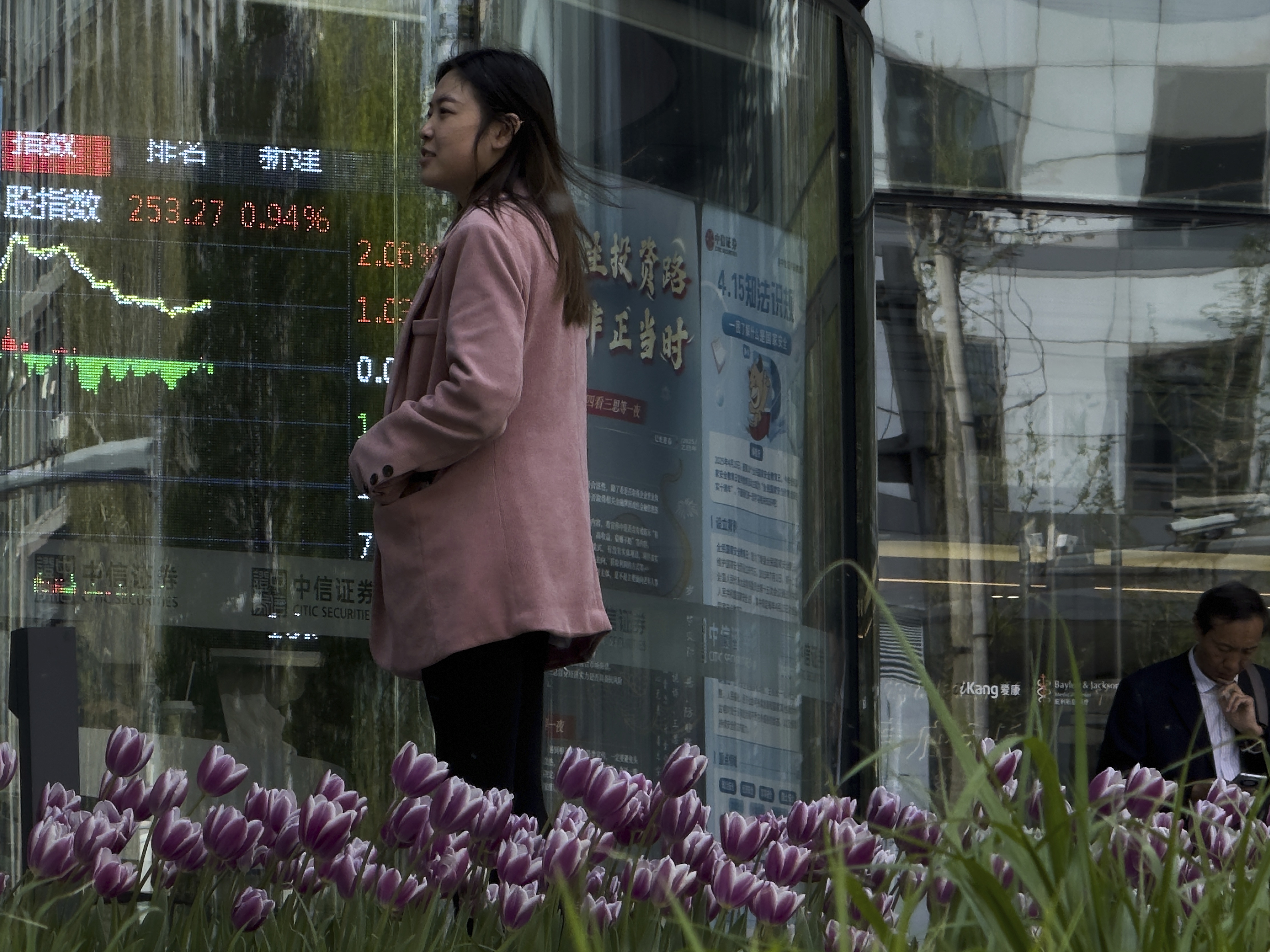 caption: People stand outside a brokerage house, as an electronic board displays shares trading, in the Central Business District in Beijing on Thursday.