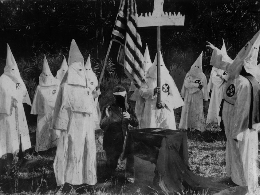 caption: Members of the Ku Klux Klan ceremonially initiate a new recruit at a meeting in 1922.