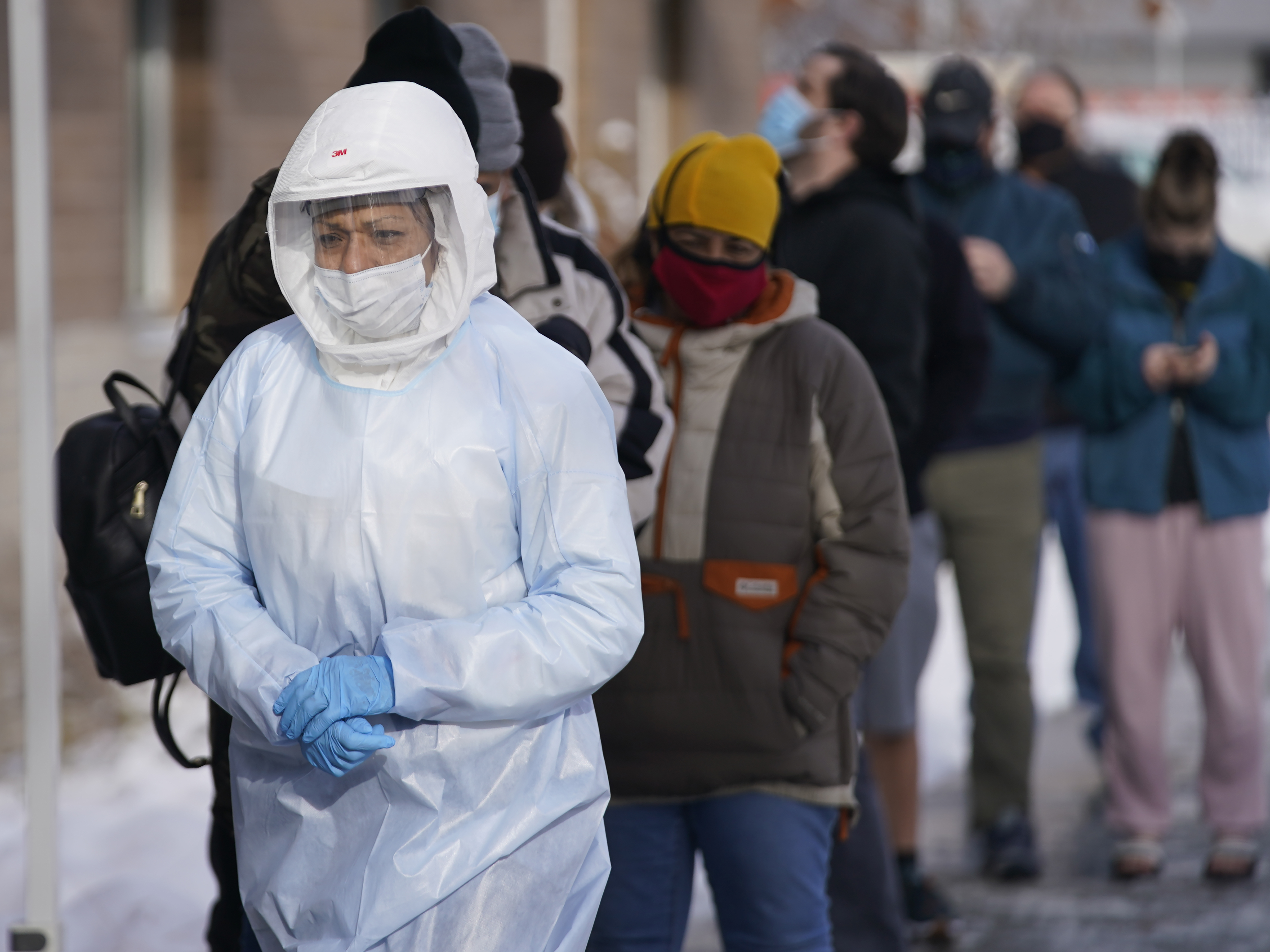 caption: A member of the Salt Lake County Health Department COVID-19 testing staff walks past a line outside the Salt Lake County Health Department, Tuesday, Dec. 28, in Utah. New CDC guidelines that shorten the isolation period for COVID-19 cases have some essential workers concerned.