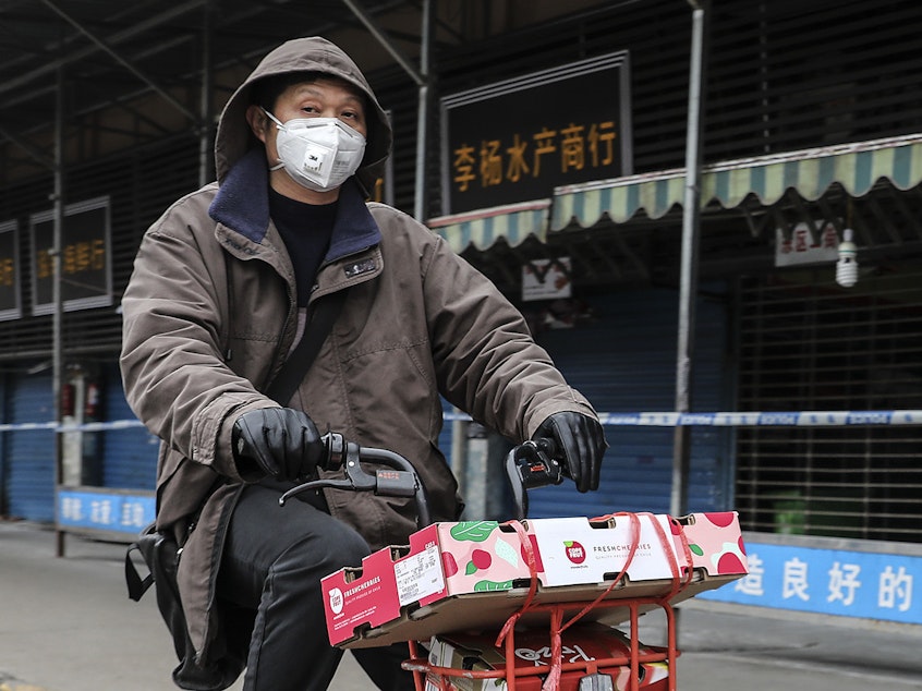 caption: A man rides past the Huanan Seafood Wholesale Market in Wuhan, China, which was closed after being linked to cases of a newly discovered coronavirus.