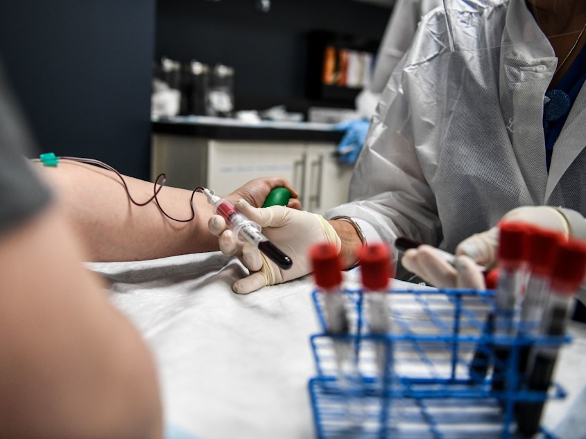 caption: A researcher takes blood samples from a patient as she participates in a COVID-19 vaccine study last month at the Research Centers of America in Hollywood, Fla.