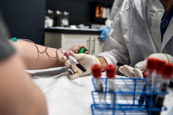 caption: A researcher takes blood samples from a patient as she participates in a COVID-19 vaccine study last month at the Research Centers of America in Hollywood, Fla.