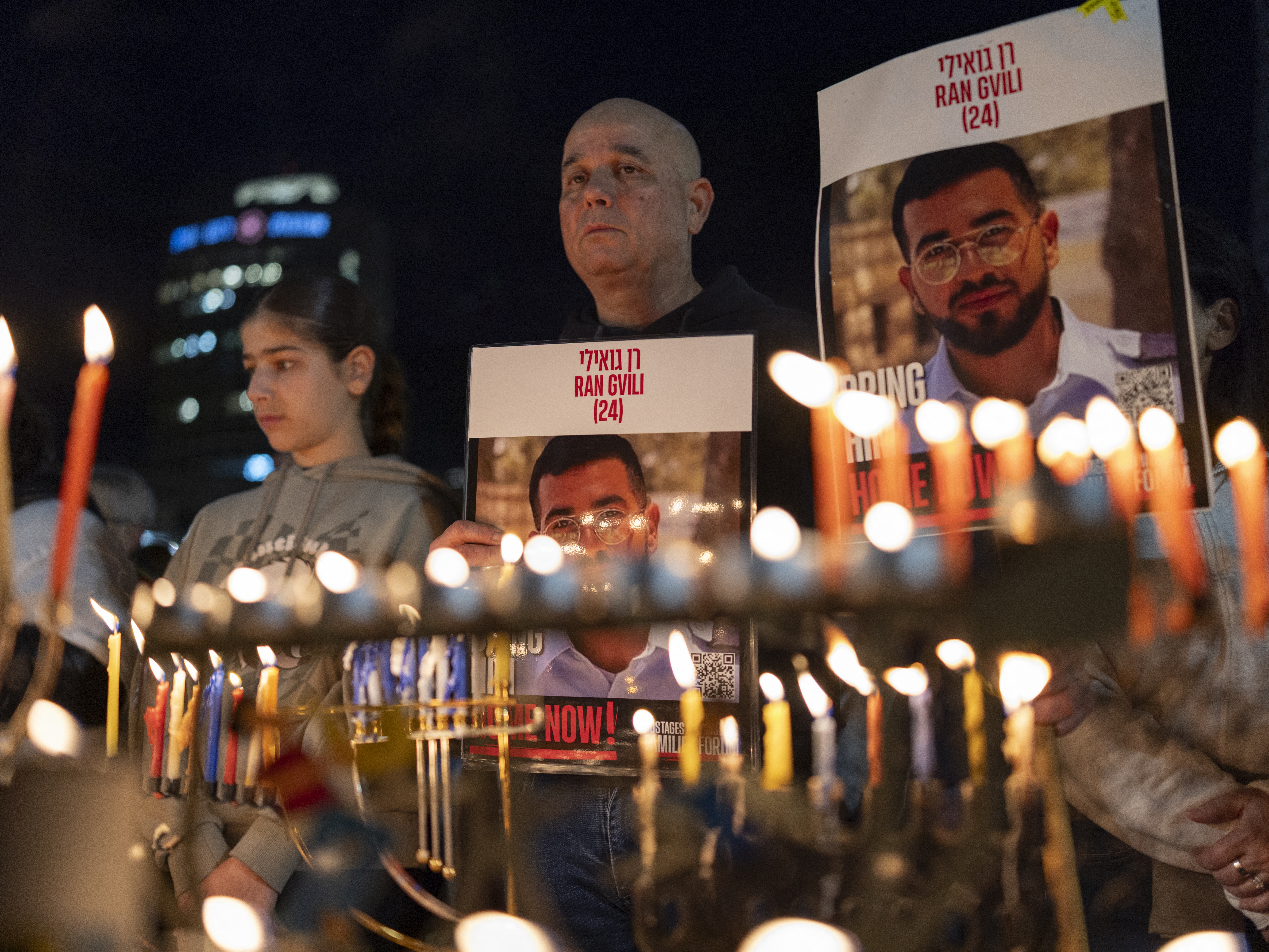 caption: Israelis light the 8th candle of Hanukkah in Hostage Square holding placards bearing the face of Ran Gvili in Tel Aviv, Israel, on Dec. 21, 2025, as they call for the return of his remains.