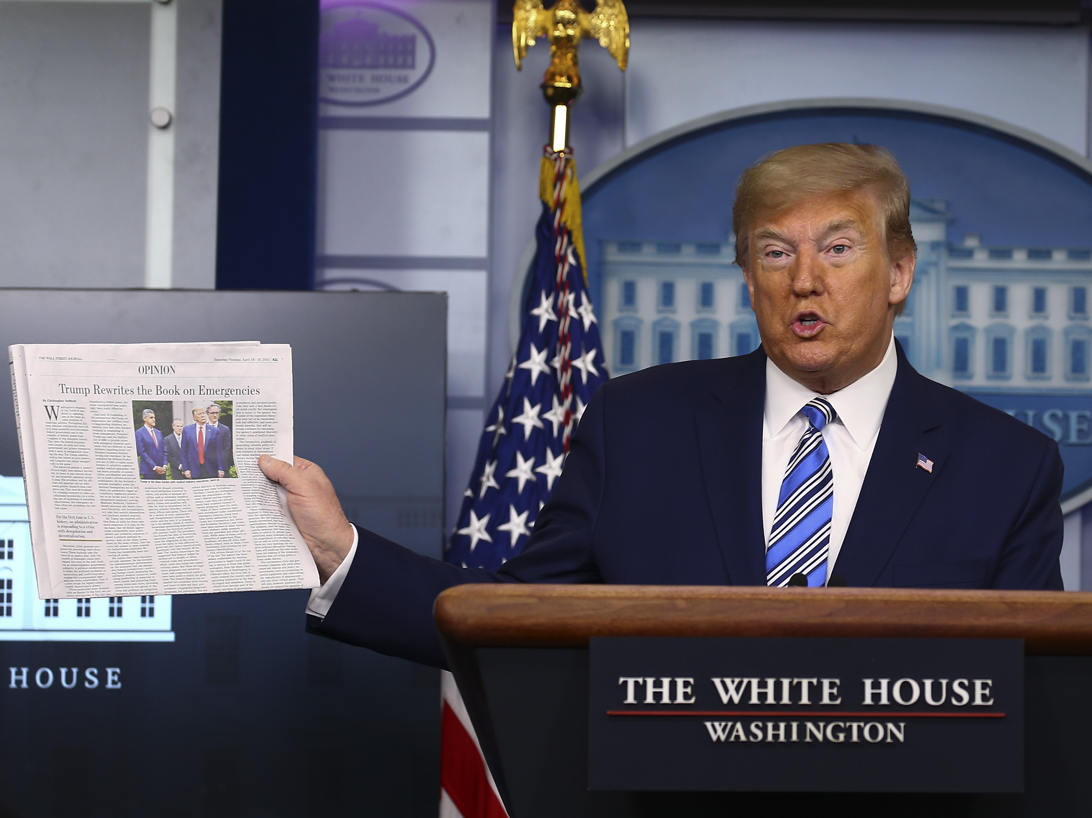 caption: Then-President Donald Trump holds up <em>The Wall Street Journal </em>as he speaks at the White House on April 19, 2020.