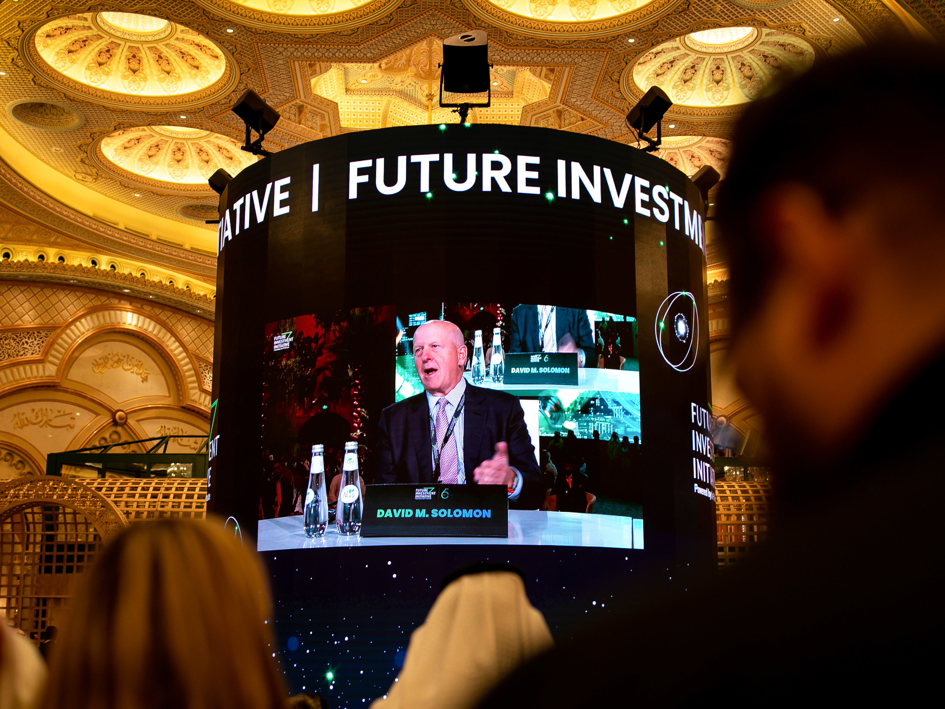 caption: Attendees watch David Solomon, chief executive officer of Goldman Sachs & Co., on a screen as he speaks during a panel session at the Future Investment Initiative (FII) conference in Riyadh, Saudi Arabia, on Tuesday, Oct. 25, 2022.