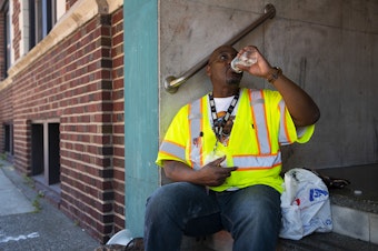caption: Construction worker David Evans takes a break in the shade during a heat wave on July 28, 2022, in Seattle's University District. 