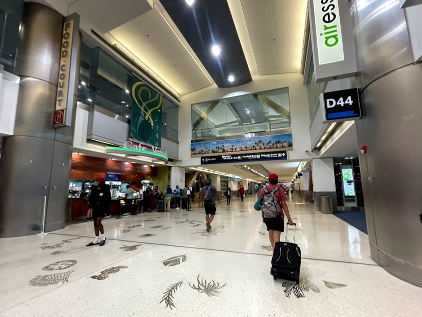 caption: Travelers make their way through SeaTac International Airport.