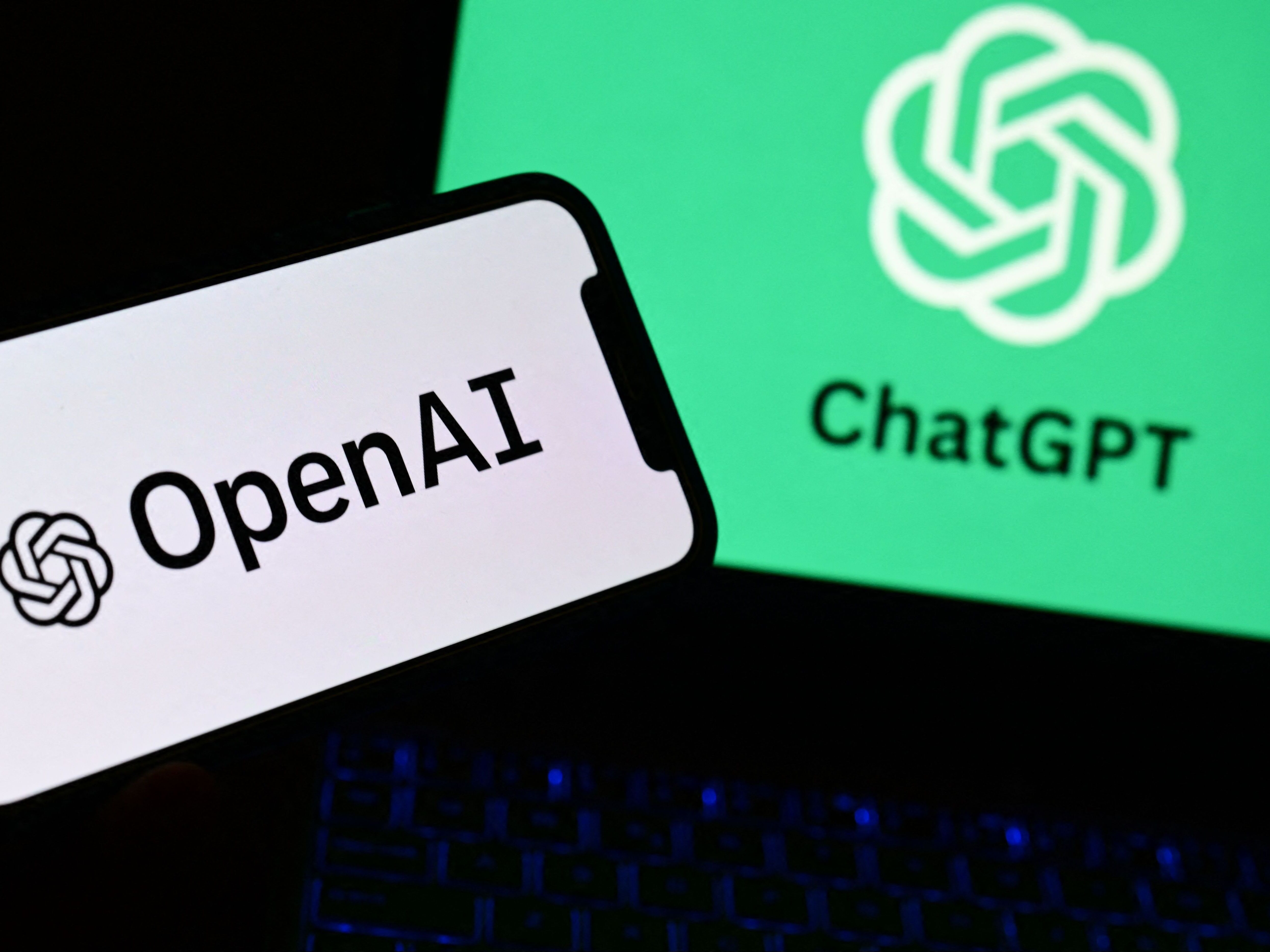 caption: A photo taken on October 4, 2023 in Manta, near Turin,  shows a smartphone and a laptop displaying the logos of the artificial intelligence OpenAI research laboratory and ChatGPT robot.