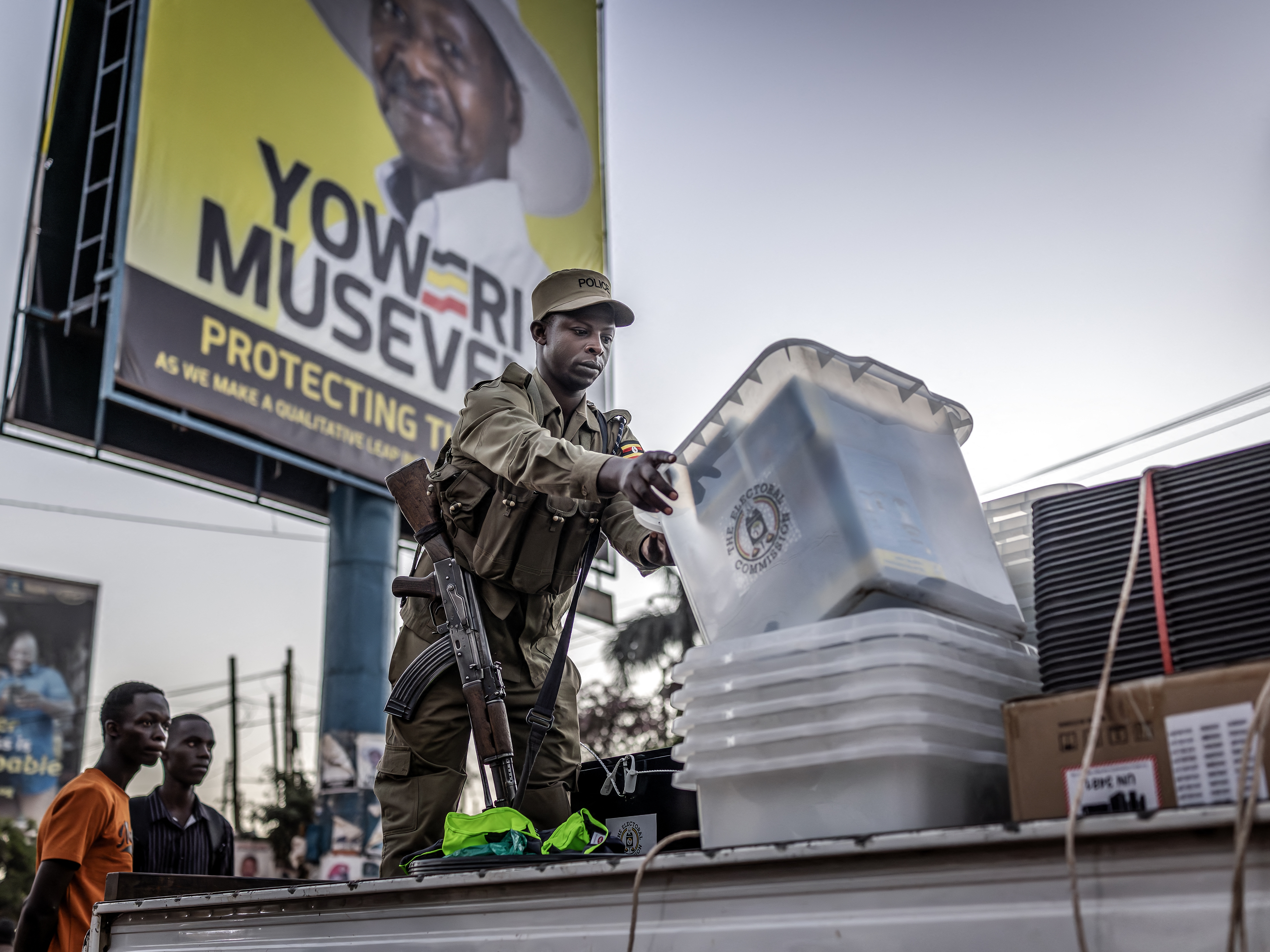 caption: A Ugandan police officer unloads ballot boxes from a truck at a polling station set up in front of an electoral billboard supporting Uganda's incumbent president Yoweri Museveni in Kampala on Jan. 15, 2026.