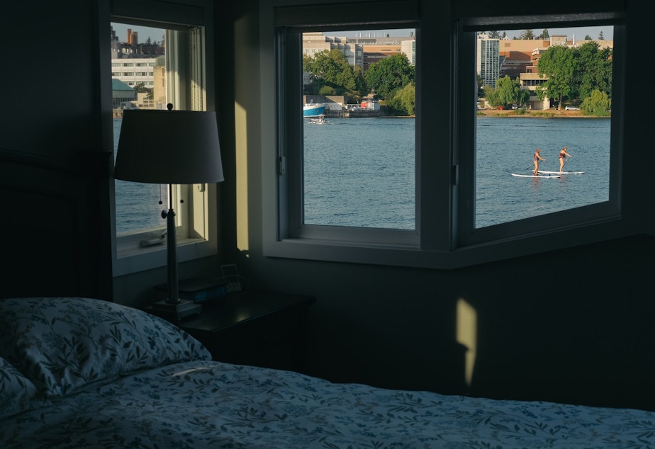 caption: Stand up paddle boarders on Portage Bay are seen passing from the bedroom window of Carol and Carl Buchan's floating home on Shelby dock, September 7, 2021.