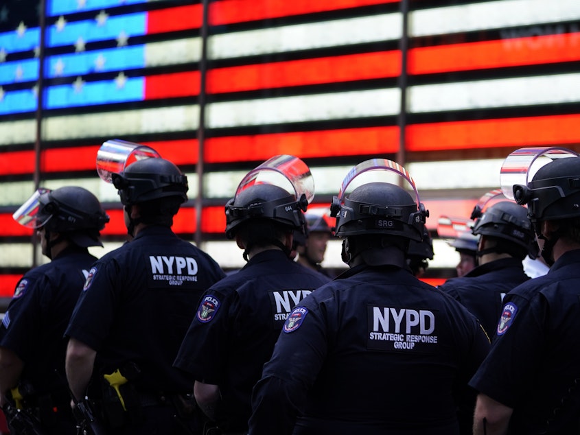 caption: New York City police officers watch demonstrators in Times Square on June 1 during a Black Lives Matter protest.