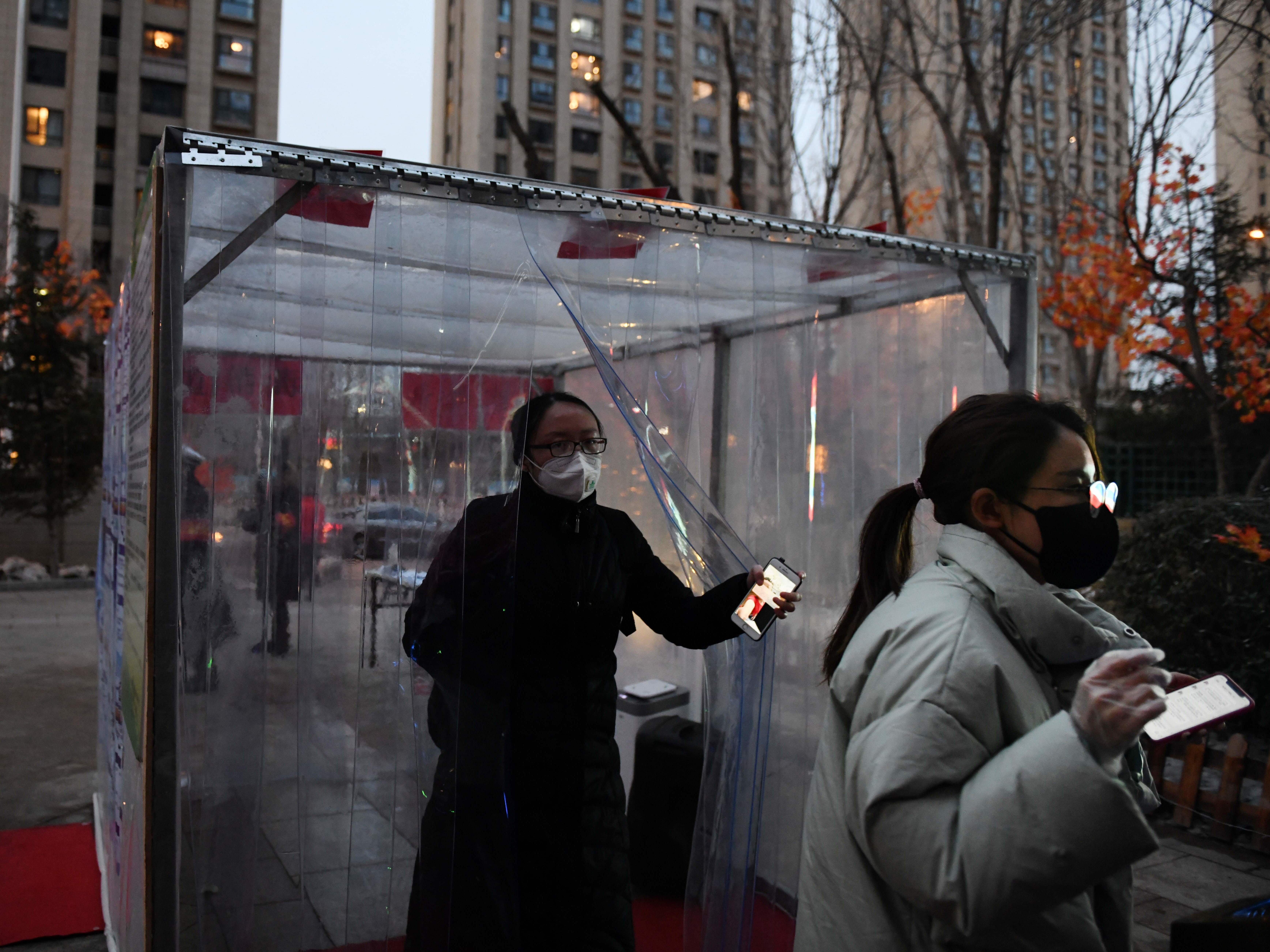 caption: Mainland China currently has more than 70,000 confirmed COVID-19 cases, according to the World Health Organization. Here, people pass through a disinfection channel set up at the entrance to their residential compound in Tongzhou, east of Beijing. The channel uses humidifiers to spray a mist of disinfectant as residents pass through.