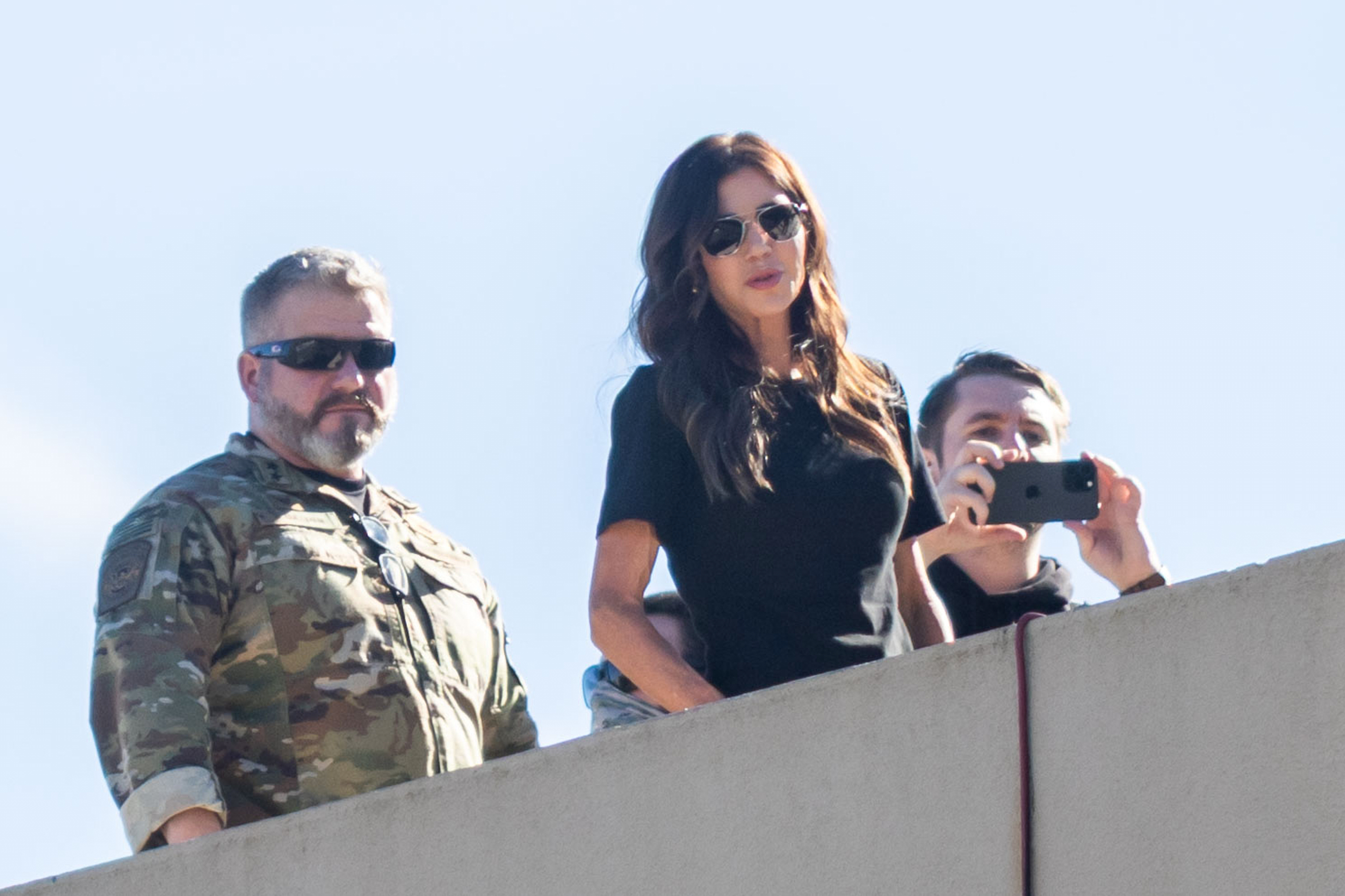 caption: U.S. Secretary of Homeland Security Kristi Noem, center, stands on the roof of a U.S. Immigration and Customs Enforcement facility in Portland, Oregon, Tuesday, Oct. 7, 2025. 