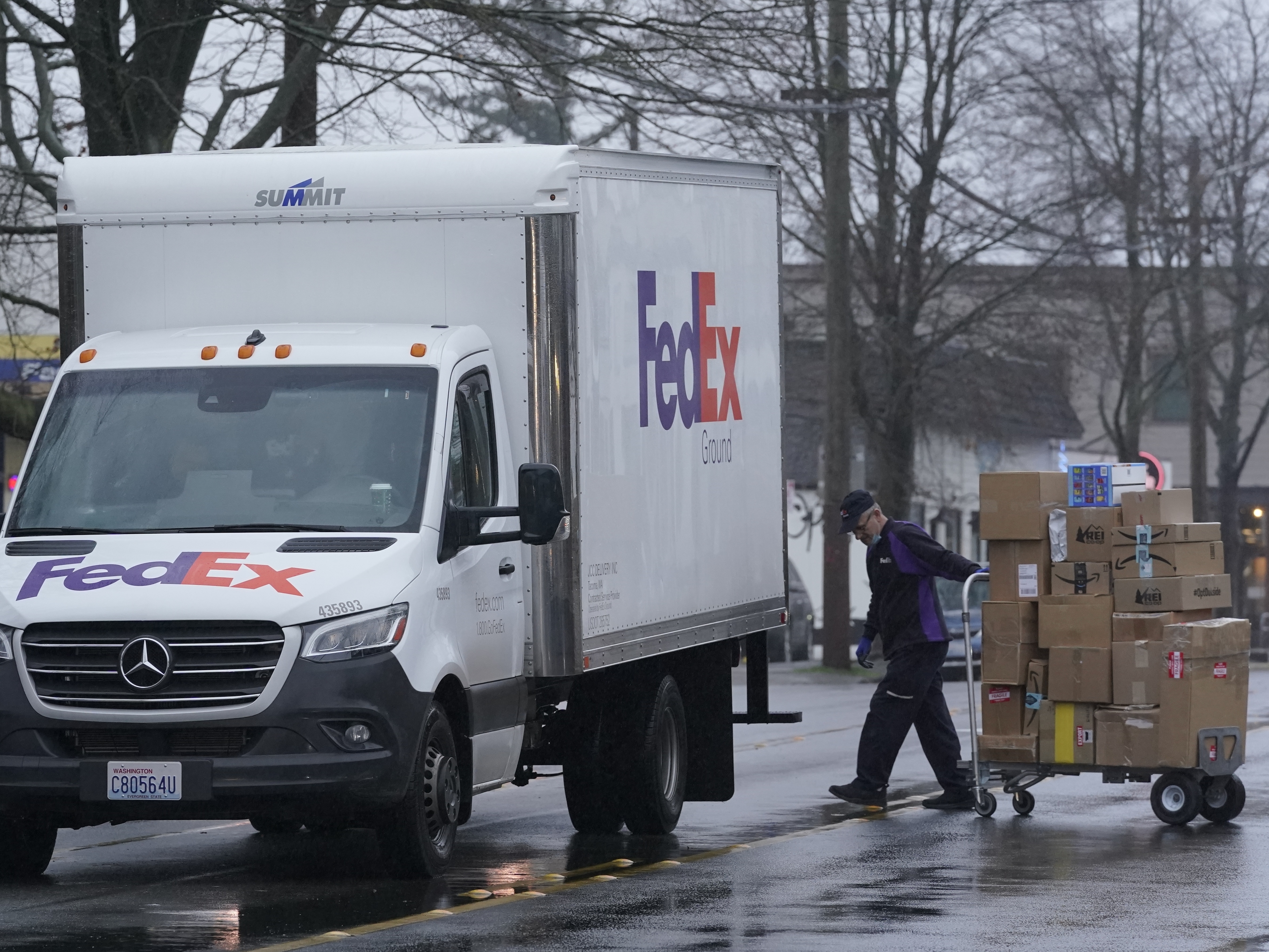 caption: A driver with FedEx carries a package away from a van in Seattle on Dec. 8, 2020. A huge increase in online shopping this year has demand for package delivery exceeding capacity this holiday season and stretching the delivery supply chain thin.