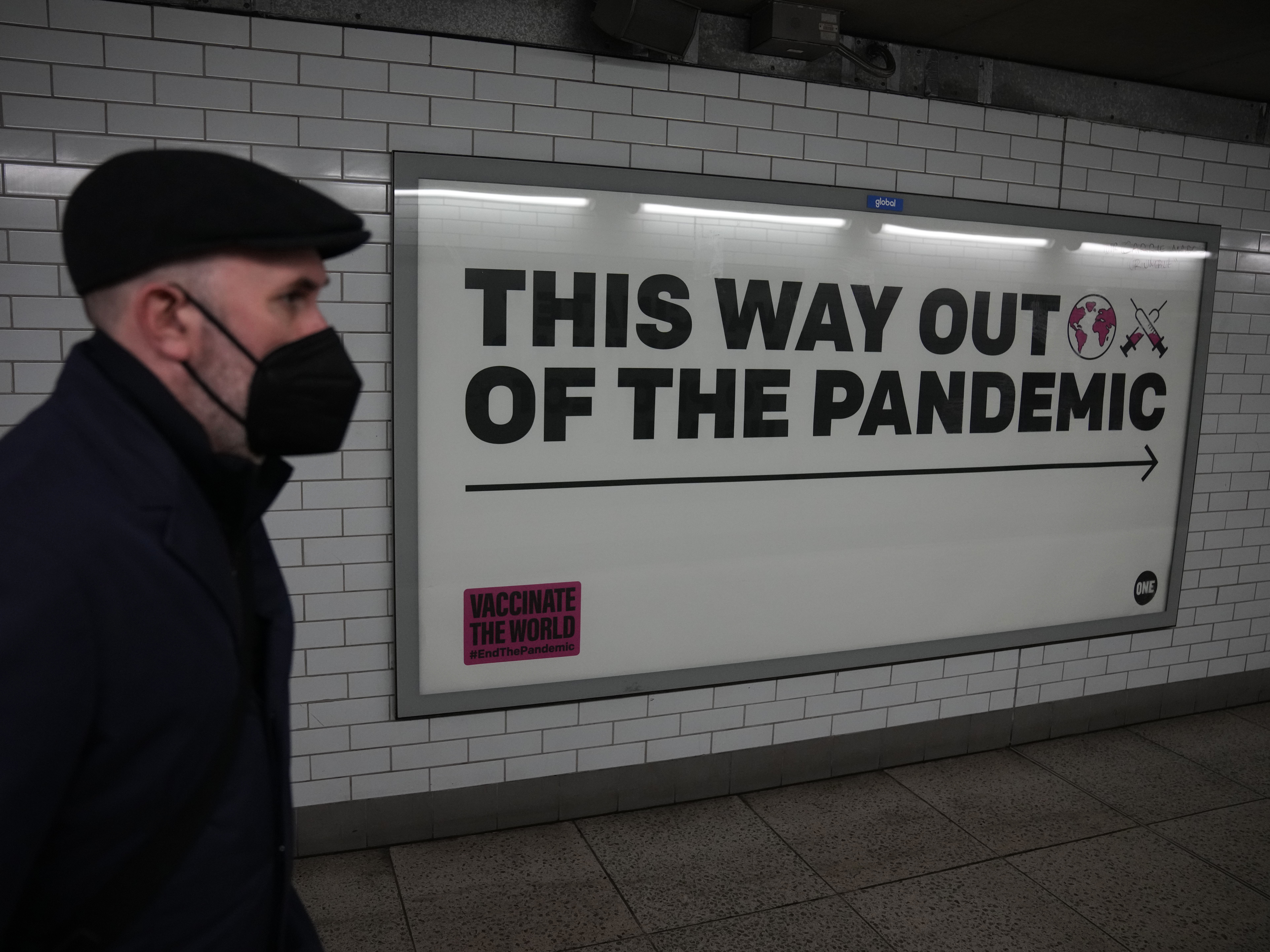 caption: A man wearing a face mask to curb the spread of coronavirus walks past a health campaign poster in the Westminster underground train station, in London.
