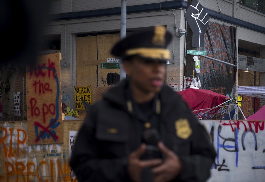 caption: A Black power fist, 'Fuck the PoPo' and Black Lives Matter signs are shown on the Seattle Police Department's East Precinct building as Police Chief Carmen Best holds a press briefing after the Capitol Hill Organized Protest zone was cleared by Seattle Police Department officers early Wednesday morning, July 1, 2020, at the intersection of 12th Avenue and East Pine Street in Seattle. 