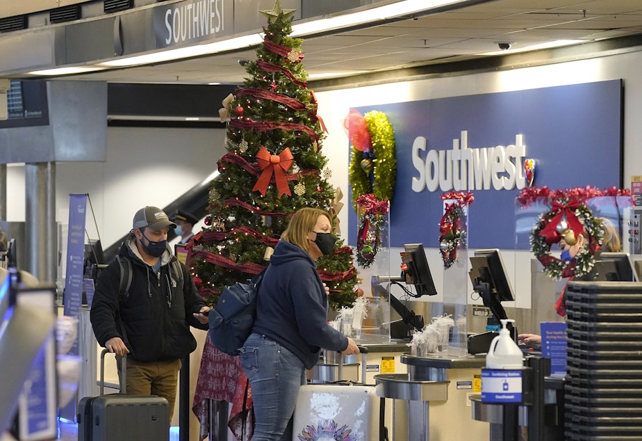 caption: Travelers wear masks as they check in next to a holiday tree at a Southwest Airlines ticket desk, Friday, Dec. 10, 2021, at Seattle-Tacoma International Airport in Seattle. 
