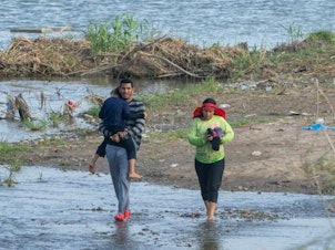 caption: Migrants walk in the water along the Rio Grande border with Mexico in Eagle Pass, Texas.