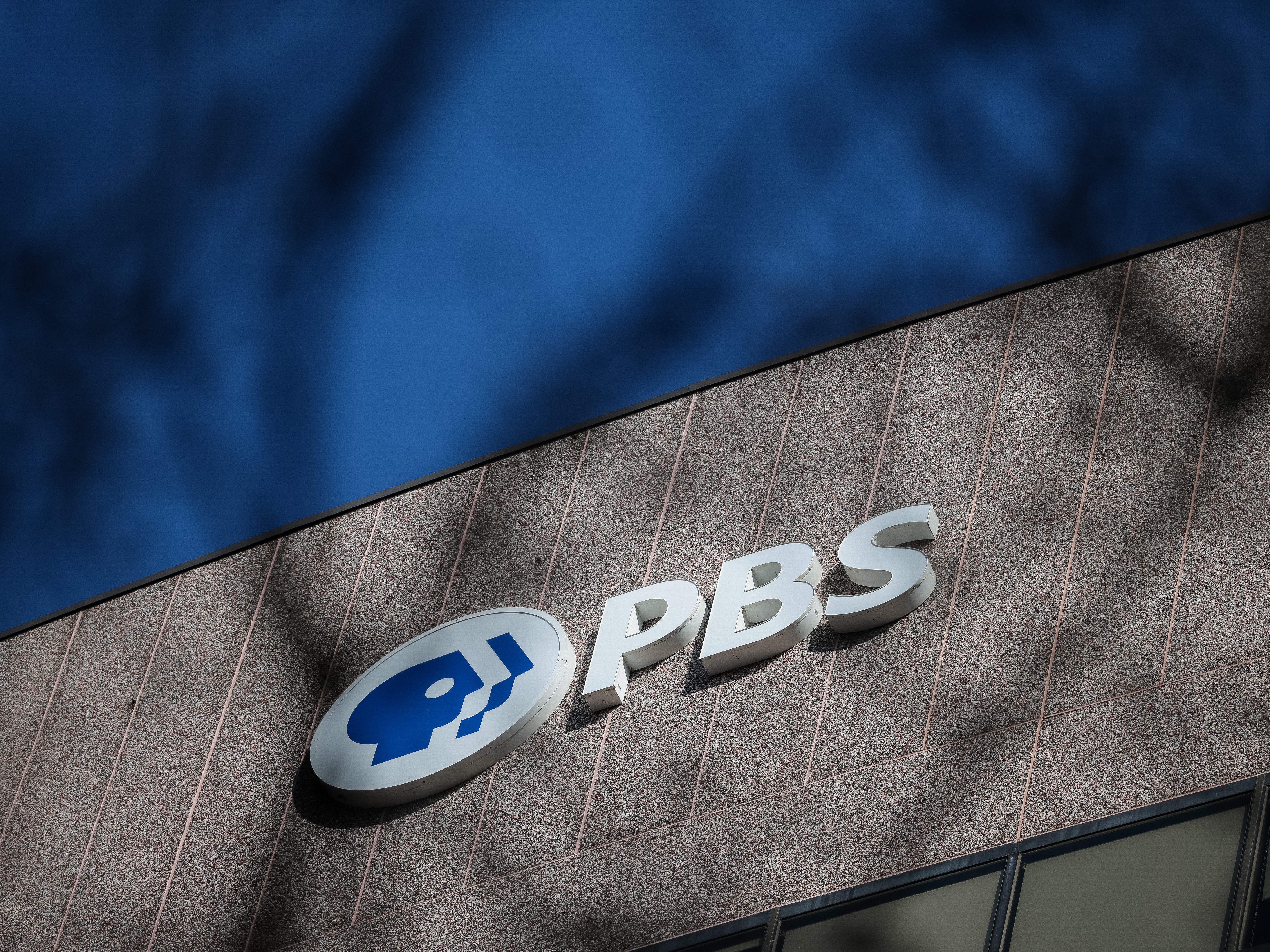caption: A sign for the Public Broadcasting Service is seen on its building headquarters on Feb. 18, 2025 in Arlington, Va.