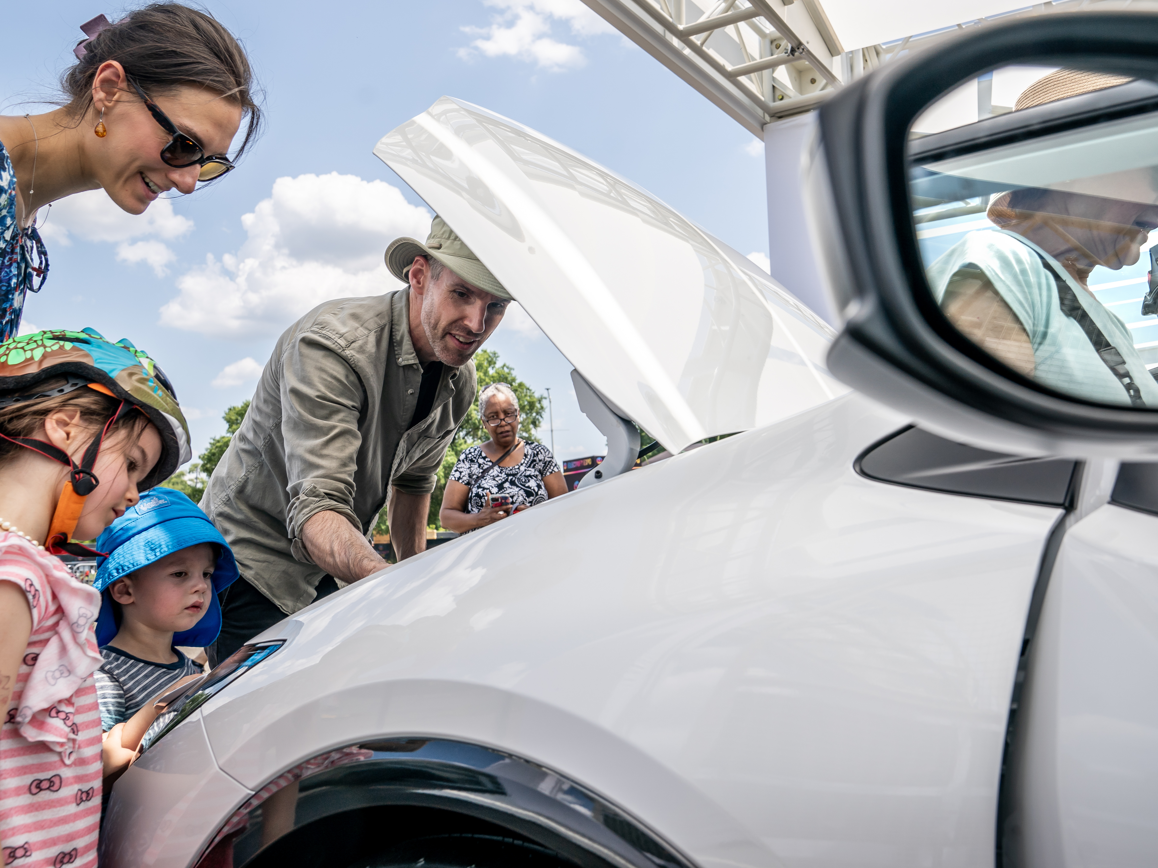 caption: A family inspects the engine of a new Toyota Prius model during the Electrify Expo In D.C. in Washington, D.C., on July 23, 2023. Getting an electric vehicle tax credit of up to $7,500 will get a lot easier next year.