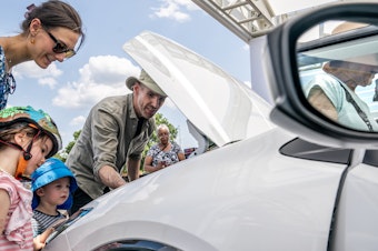 caption: A family inspects the engine of a new Toyota Prius model during the Electrify Expo In D.C. in Washington, D.C., on July 23, 2023. Getting an electric vehicle tax credit of up to $7,500 will get a lot easier next year.