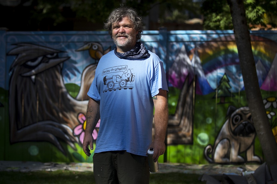 caption: Ryan Henry Ward stands for a portrait in front of a mural that he is working on in the backyard of a home on Wednesday, September 8, 2021, in Shoreline.