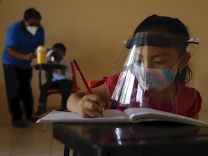 caption: Wearing a mask and a face shield to curb the spread of the coronavirus, 10-year-old Jade Chan Puc writes in her workbook during the first day of class in Hecelchakán, Campeche state, Mexico, on April 19. On average, schools in Latin America and the Caribbean were closed longer than any in any other region, according to UNICEF.