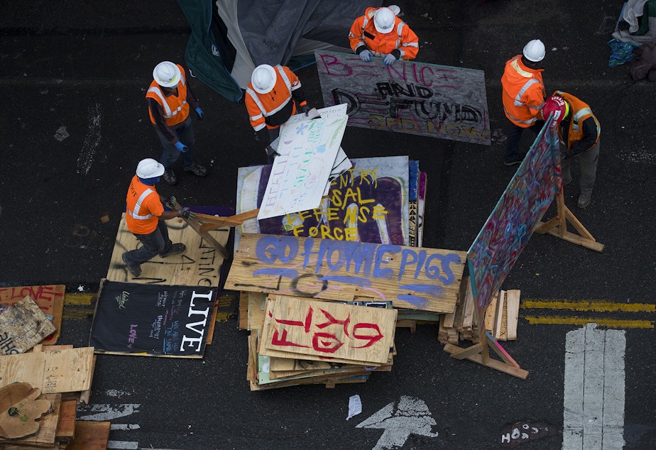 caption: Seattle Department of Transportation employees remove items from outside of the East Precinct building after the Capitol Hill Organized Protest zone was cleared by Seattle Police Department officers early Wednesday morning, July 1, 2020, in Seattle.