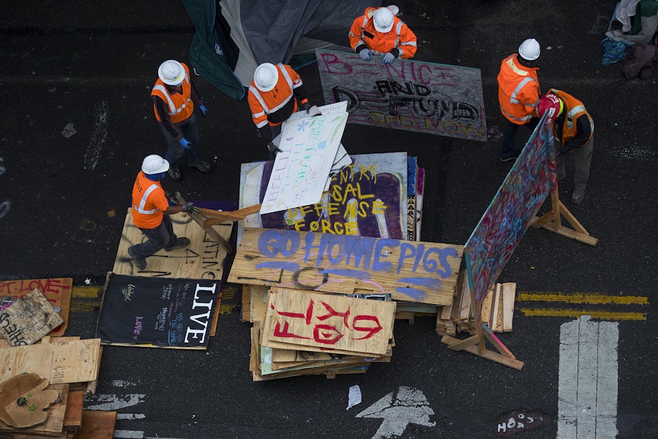 caption: Seattle Department of Transportation employees remove items from outside of the East Precinct building after the Capitol Hill Organized Protest zone was cleared by Seattle Police Department officers early Wednesday morning, July 1, 2020, in Seattle.