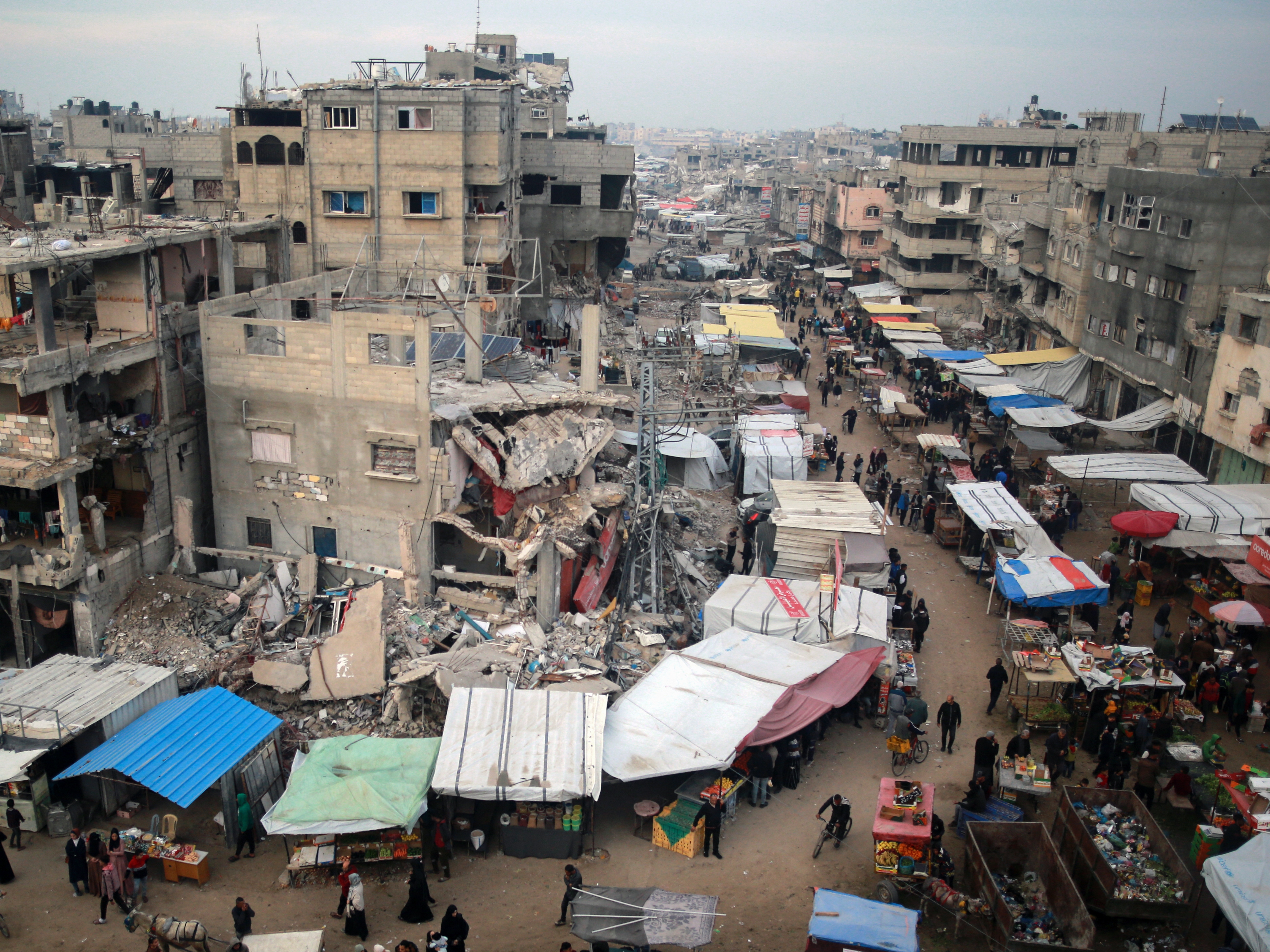 caption: People walk past stalls selling goods amid the rubble of buildings destroyed in Israeli strikes, in Khan Younis in the southern Gaza Strip on Wednesday.