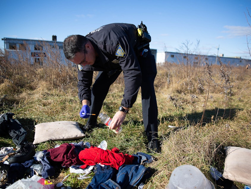 caption: Officer Christian Bruckhart collects used needles from a vacant site in his patrol area in New Haven, Conn.