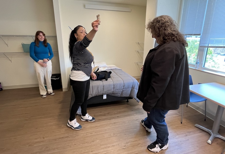 caption: Plymouth Housing case manager Angel Cezear smudges the room with burning sage, at the request of new resident Kevin Thomas Kiso (right) as his Salvation Army caseworker, Katy Cossette (left) looks on.