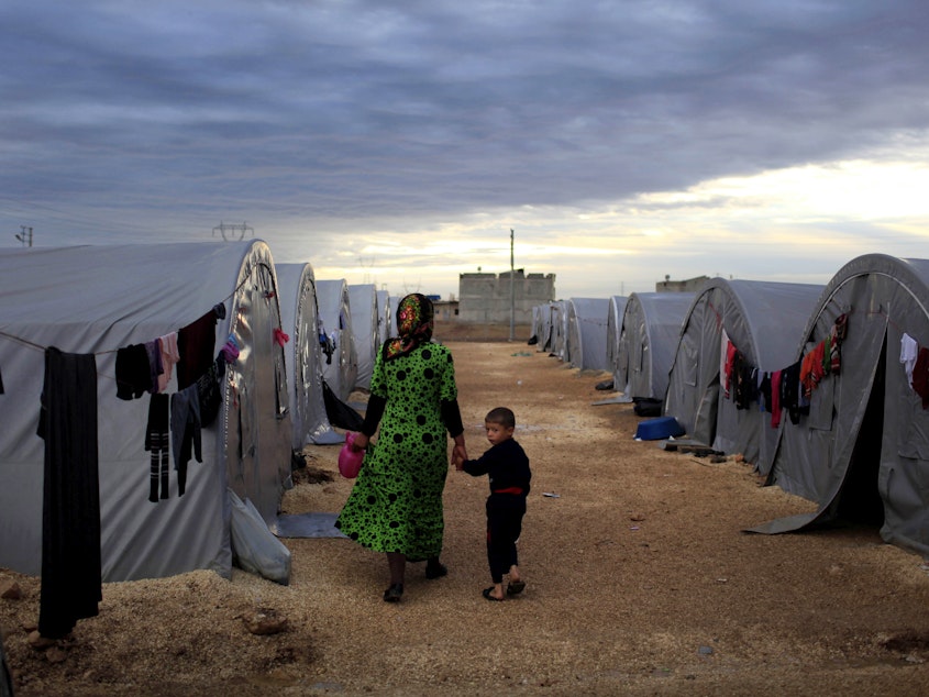 caption: A Kurdish refugee mother and son from the Syrian town of Kobani walk beside their tent in a camp in the Turkish town of Suruc on the Turkish-Syrian border in 2014. President-elect Joe Biden aims to reverse the Trump administration's dramatic cuts to refugee admissions.