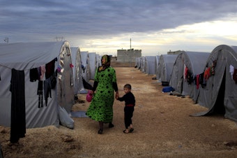 caption: A Kurdish refugee mother and son from the Syrian town of Kobani walk beside their tent in a camp in the Turkish town of Suruc on the Turkish-Syrian border in 2014. President-elect Joe Biden aims to reverse the Trump administration's dramatic cuts to refugee admissions.