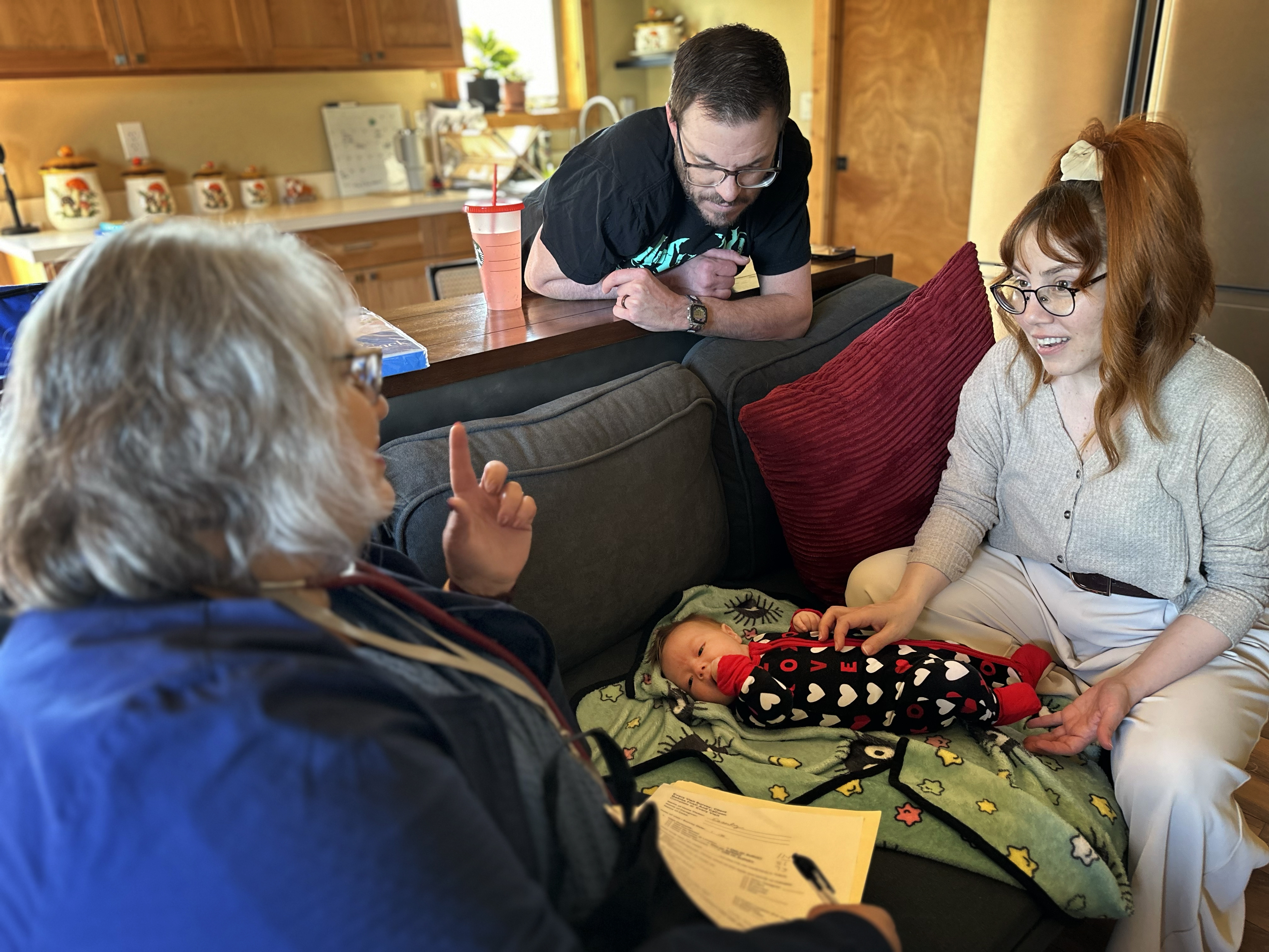 caption: Barb Ibrahim, left, drove half an hour to visit Amber and Matt Luman and their new daughter, Esserley. Ibrahim, a nurse of more than 30 years, is part of new program in Oregon that offers free home visits from a registered nurse for any family with a newborn.