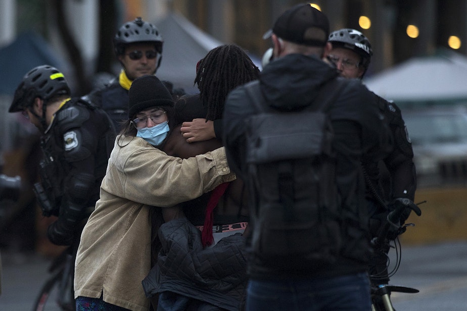 caption: Protesters embrace at a Seattle Police Department line outside of the Capitol Hill Organized Protest zone after the zone was cleared by Seattle Police Department officers early Wednesday morning, July 1, 2020, in Seattle.