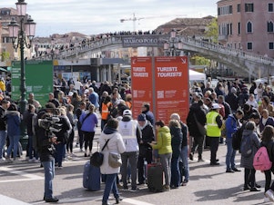 caption: Stewards check tourists' QR code access outside the main train station in Venice, Italy, on Thursday.